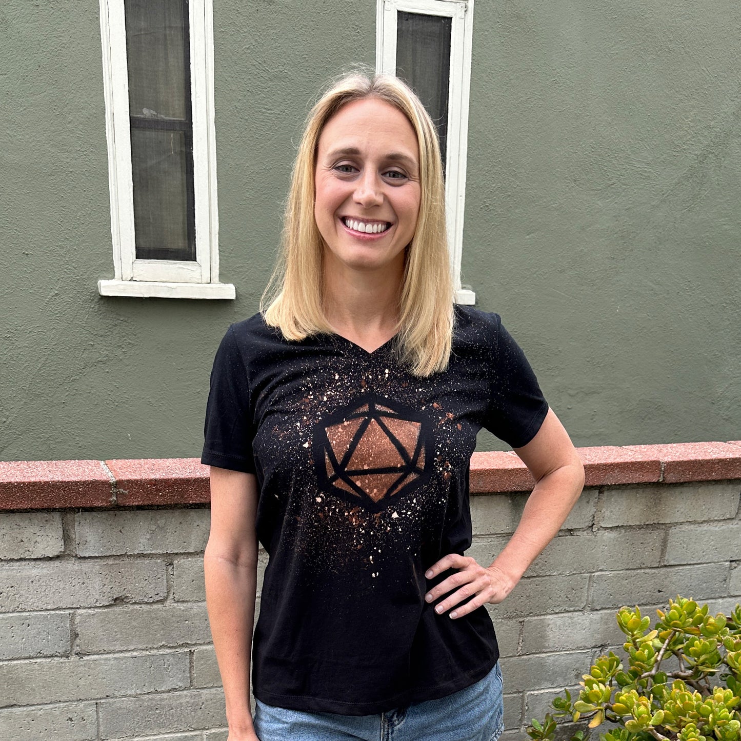 Amy Vorpahl smiling with her hand on her hip. She's wearing a black tshirt with a D20 die design made out of bleach splatters