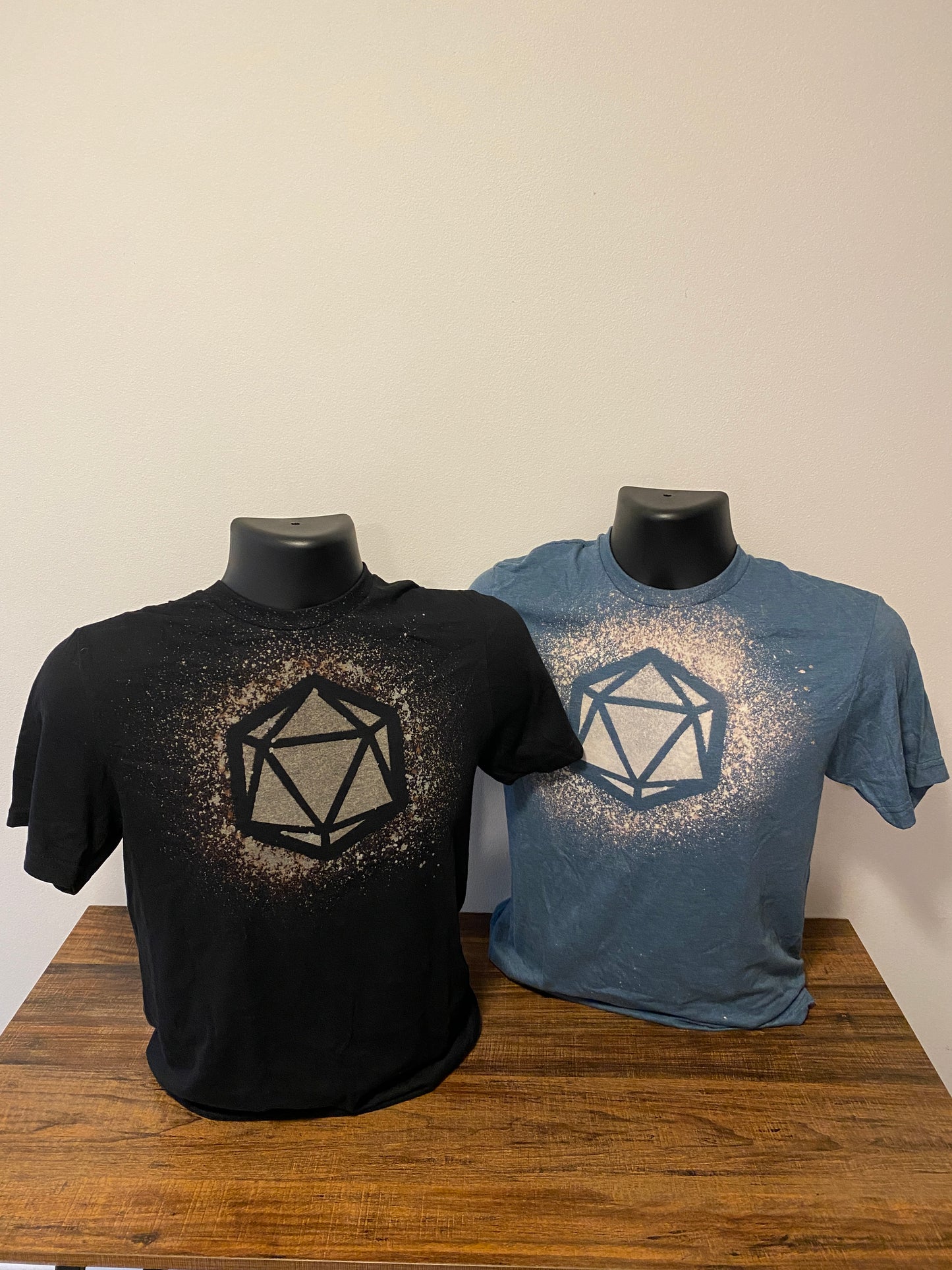 one black and one blue tee shirt with a D20 design, made with bleach. They are sitting on shirt forms, side by side