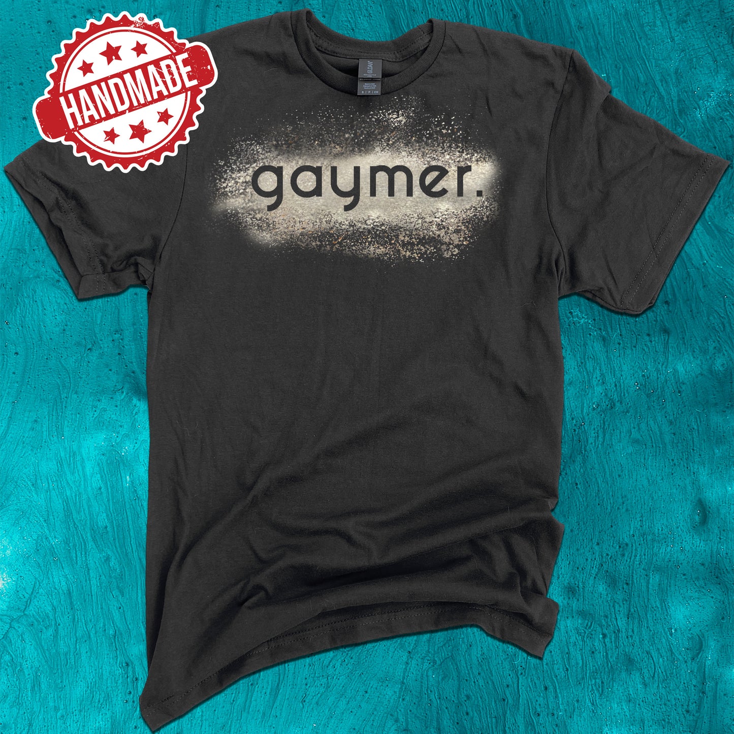 Black shirt on a green background that says "gaymer" surrounded by bleach splatter design