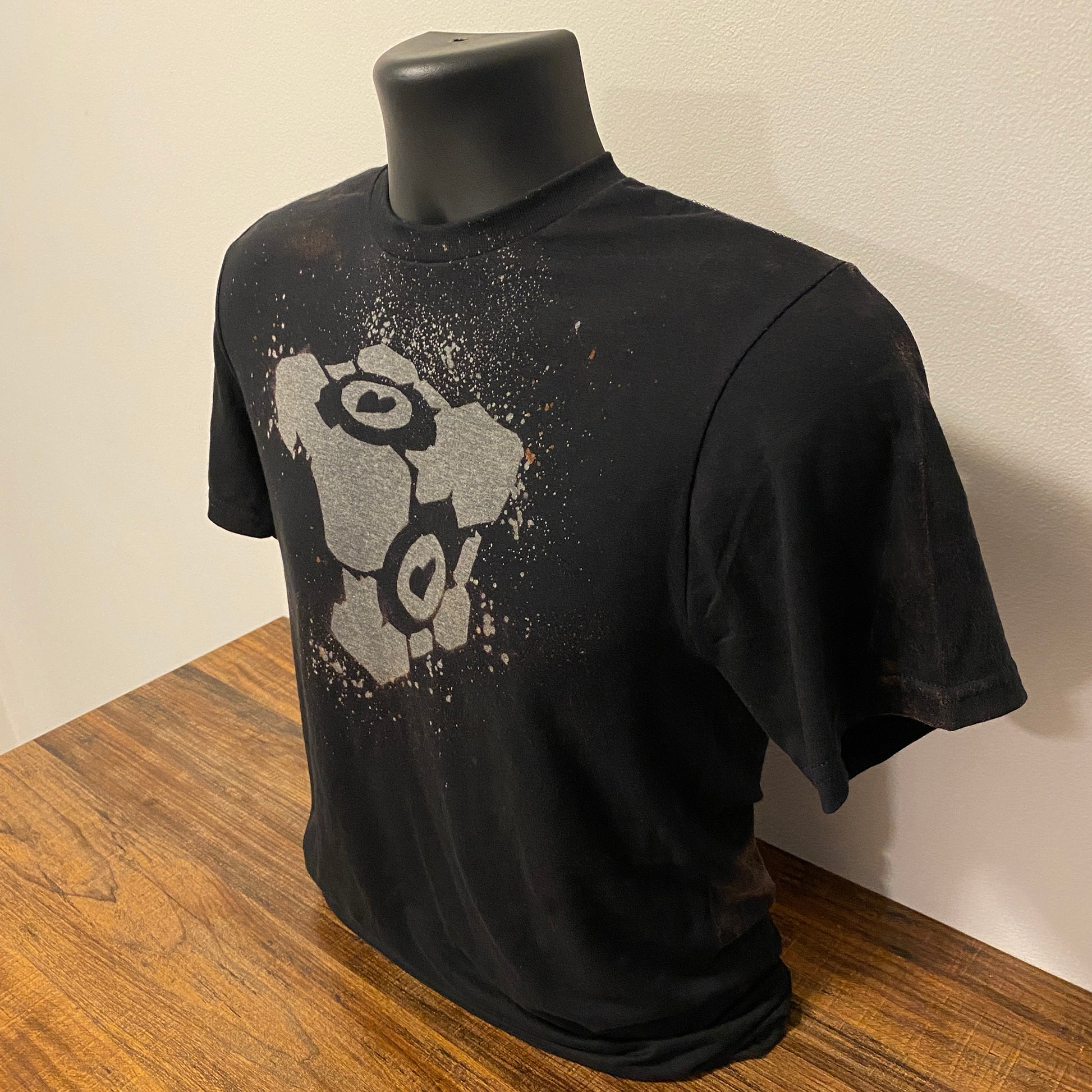 Black shirt with a Portal Companion Cube design made with bleach on a shirt form