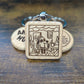square wooden keychain with an engraved image of the "this is fine" dog in a house on fire 