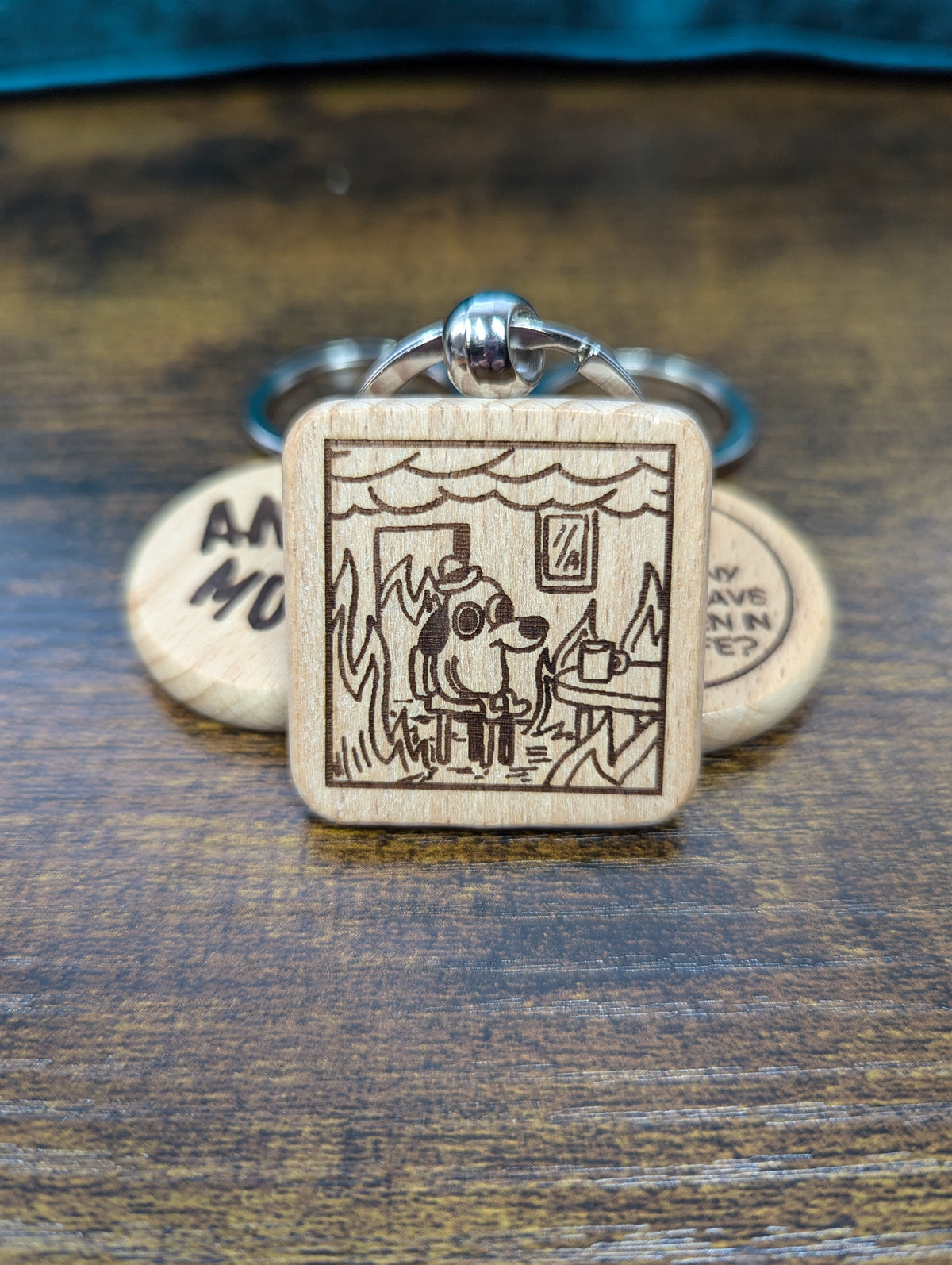 square wooden keychain with an engraved image of the "this is fine" dog in a house on fire 