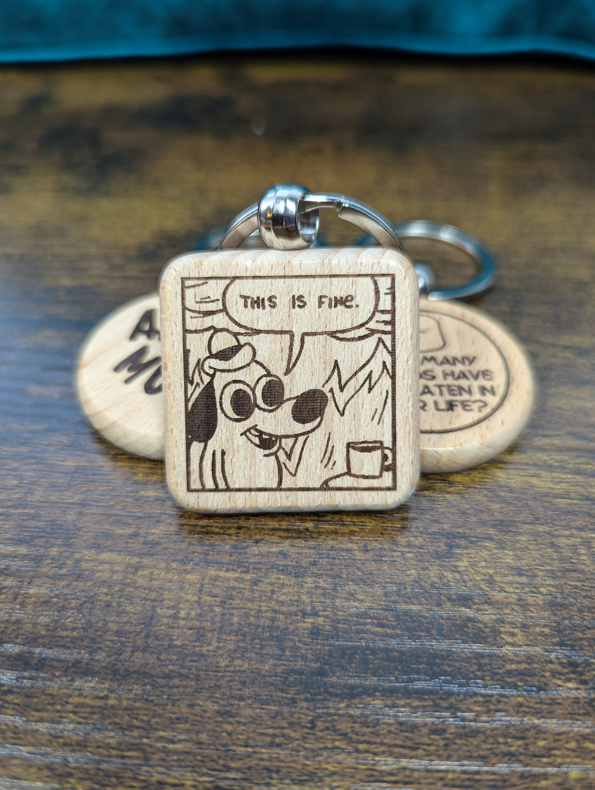 square wooden keychain with an engraved image of the "this is fine" dog in a house on fire 
